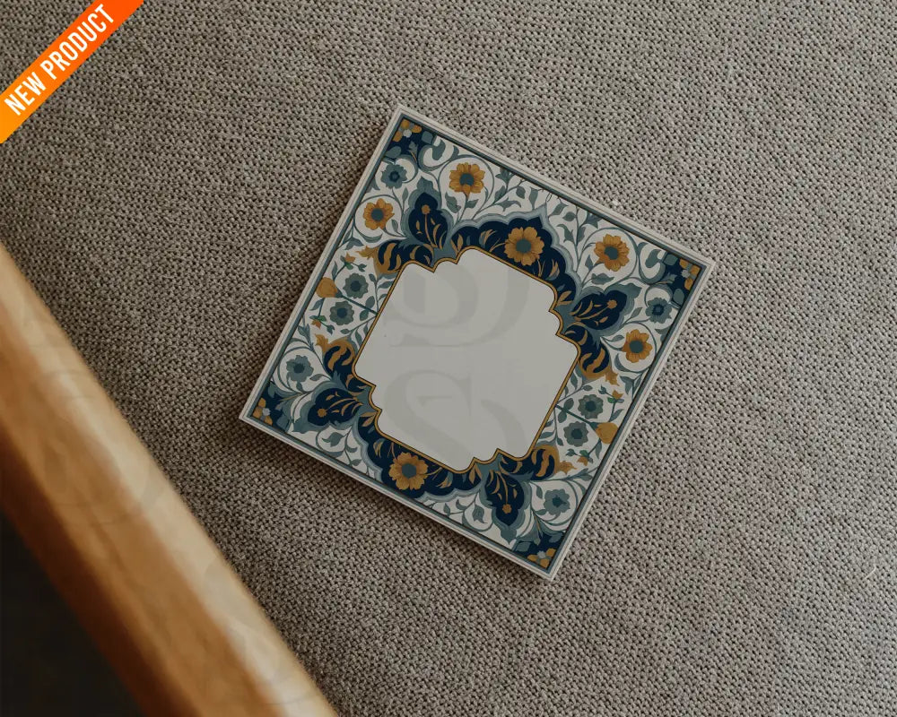 Square wedding card with midnight blue and gold Mughal floral frame placed on a textured fabric surface in a flatlay style.