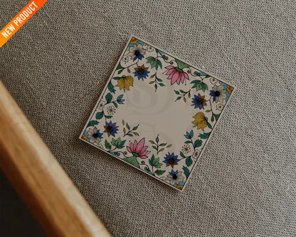 Square wedding card with a Mughal floral frame placed on a textured beige fabric in a flatlay presentation.